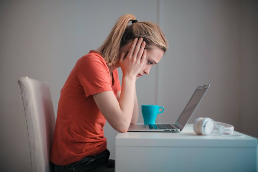 A woman looks at her work laptop with her head in her hands, clearly stressed.